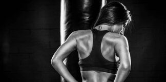 හෙට එච්චර පැහැදිලි නෑ Muscular young woman posing in front of a punching bag, on dark background